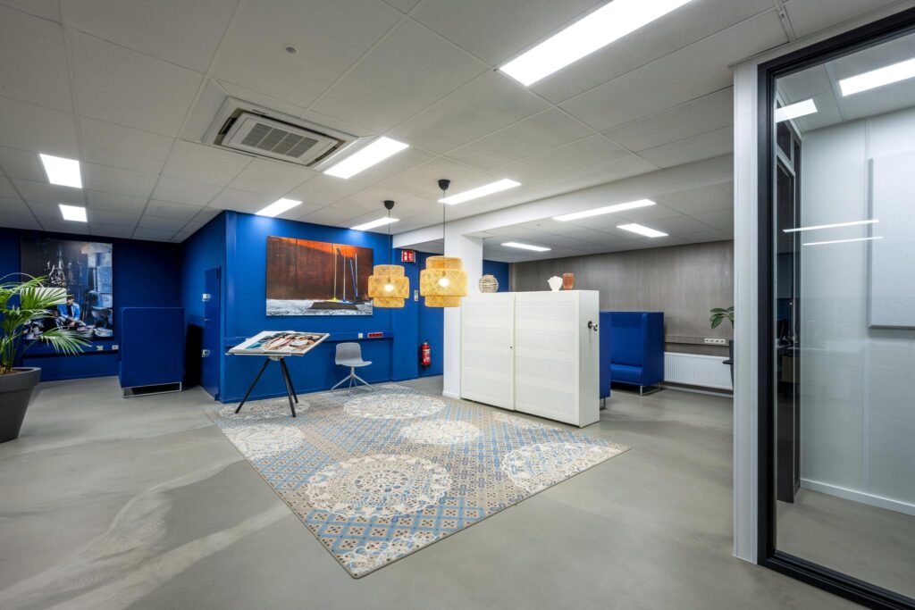 Modern ingerichte kantoorlobby aan de Van der Madeweg met blauwe wanden, kunst aan de muur, een kleurrijk vloerkleed en zitgelegenheid.